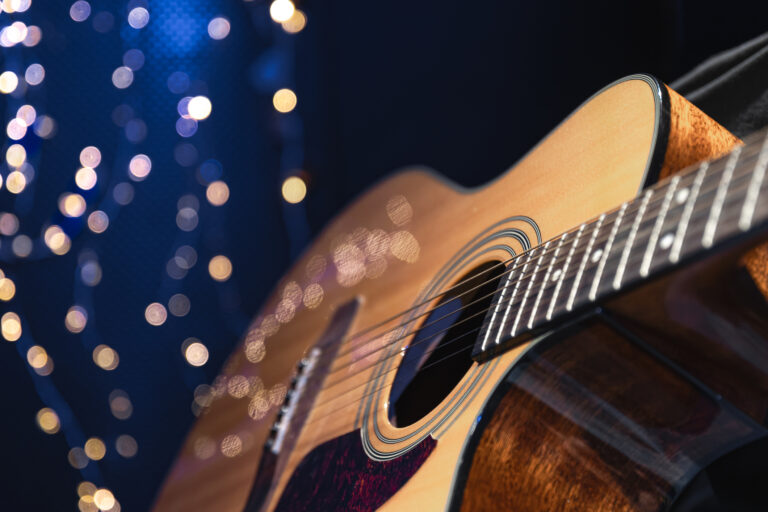 Close-up, acoustic guitar on a dark background with bokeh lights.